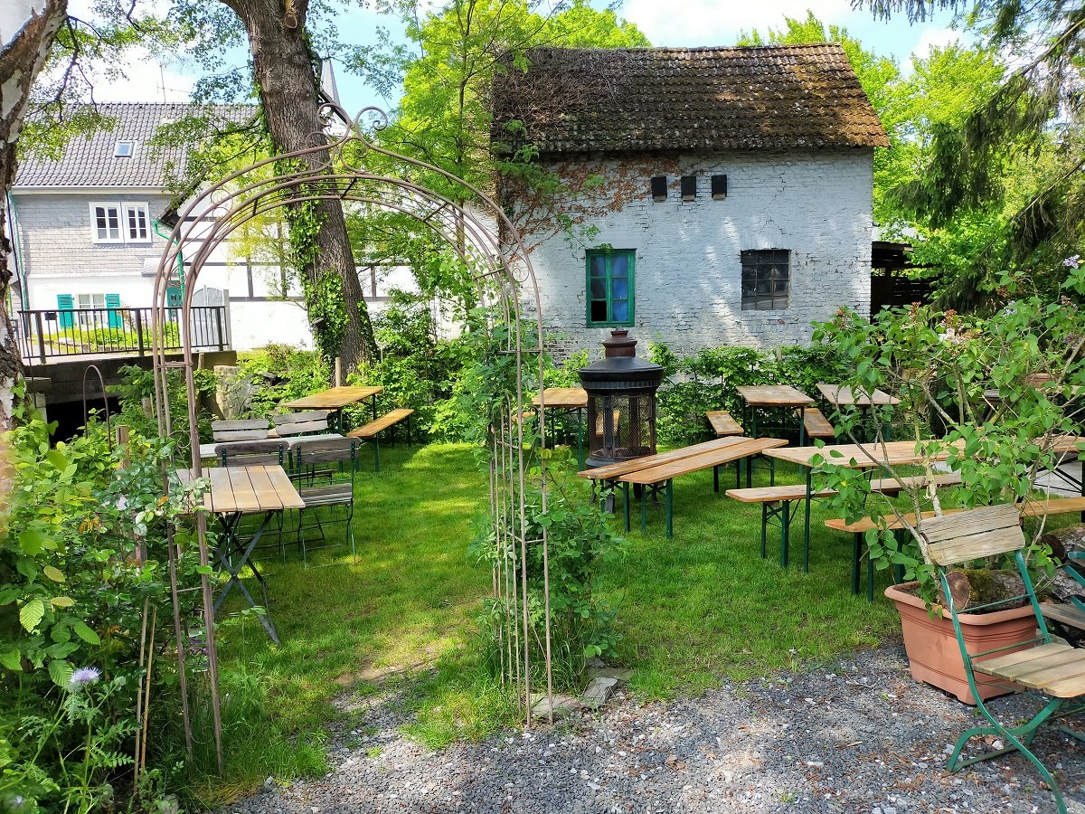 Gartentische unter Bäumen vor historischen Häusern in Gruiten